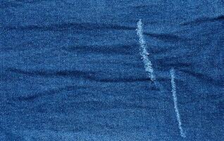 Fragment of blue jeans fabric with a hole, full frame, close up photo