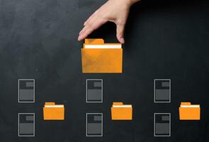 A hand holds a yellow folder over a black background with several folders and documents scattered around. Concept of control and systematization of documents photo