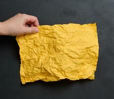 A woman's hand holds a yellow crumpled sheet of paper photo