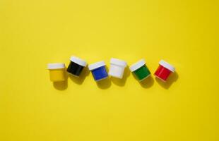 Plastic jars with multi-colored gouache on a yellow background, copy space photo