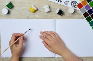 Set of watercolor paints, brushes and paper with different strokes and colors. Female hands holding a brush photo