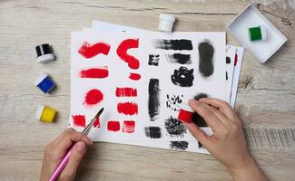 Set of watercolor paints, brushes and paper with different strokes and colors. Female hands holding a brush photo