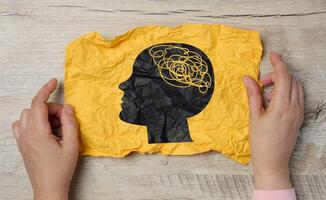 A female hand holds a crumpled paper with a black silhouette of a person's head and tangled threads inside, representing the concept of human mental health photo