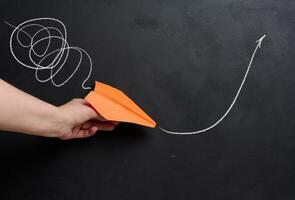 A hand holds a paper airplane with a drawn flight trajectory on the board, representing the concept of support and mentorship, providing assistance photo