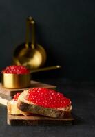 Red caviar on slices of white wheat bread on a black table, concept of luxury and gourmet cuisine photo