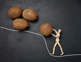 A wooden mannequin rolls a coconut up a mountain. Concept of hard work, determination and perseverance photo