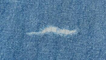 Fragment of blue jeans fabric with a hole, full frame, close up photo