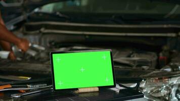 Close up shot of tablet placed on working bench in busy garage next to professional tools while technician mends vehicle. Mockup device in repair shop with meticulous specialist working in background video