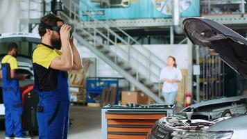 Qualified serviceman in auto repair shop using virtual reality goggles to visualize car components in order to fix them. Expert wearing modern vr headset while working on damaged vehicle video