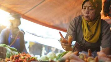 vegetal vendedor musulmán Indonesia mujer con Pañuelo es servicio clientes en el mercado. comestibles vendedor. vendedor mujer en el tradicional mercado foto