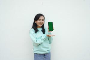 Portrait Indonesian beautiful woman wearing light blue sweater with happy and smile face show green screen mobile phone isolated on white background photo