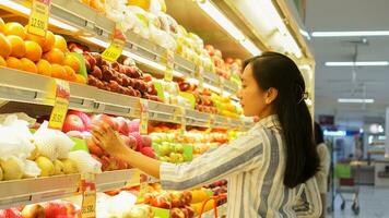 portrait of a beautiful Asian or Indonesian woman buying fruit arranged on fruit rack in a supermarket photo