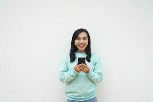 Portrait Indonesian beautiful woman wearing light blue sweater with happy and smile face look at mobile phone isolated on white background photo