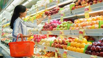 retrato de un hermosa asiático o indonesio mujer comprando Fruta arreglado en Fruta estante en un supermercado foto