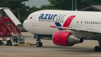 PHUKET, THAILAND FEBRUARY 25, 2023 - Commercial plane Boeing 767, RA73032 of Azur Air on the airfield of Phuket Airport. Tractor towing airliner on runway. Tourism and travel concept video