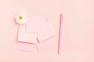 The concept is pink. Blank square small writing sheets, chrysanthemum and a pen on a pink background. Top view photo