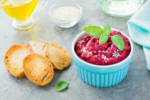 Homemade baked beet hummus in a bowl with sesame seeds and basil and baked small toast on the table photo