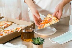 Takeout food. A woman puts a slice of pizza in a disposable plastic plate and a box of pizza on the table in the kitchen. photo