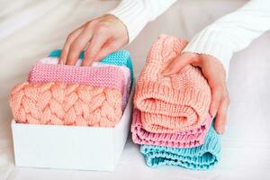Organization and order. Female hands fold knitted clothes in a pile next to a box with neatly folded things photo