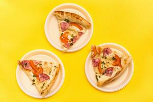 para llevar y entrega. Tres piezas de Pizza en desechable el plastico platos en un amarillo antecedentes. almuerzo para un grupo de amigos foto