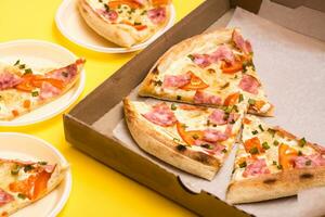 para llevar y entrega. Pizza en un cartulina caja y piezas de Pizza puesto fuera en desechable platos en un amarillo antecedentes foto