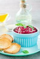 Homemade baked beetroot hummus in a bowl with sesame seeds and basil and baked small toast on a plate on the table. Vertical view photo