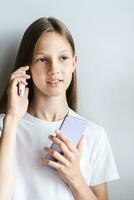 Smiling teen girl talking on a push-button telephone and holding a smartphone in her hand photo