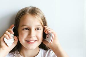 alegre niña es hablando en dos presionar el botón Los telefonos en un ligero antecedentes foto