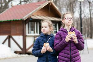 Two girls sisters eat pies bought in a food truck in a city park. Takeaway food photo