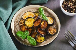 Pieces of fried eggplant with spices and basil on a plate on the table photo