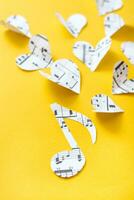 Musical notes, clef and hearts cut from paper with musical text on yellow background. Vertical view photo