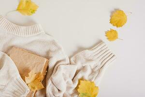 Autumn concept knitted sweater, old book and yellow leaves top view photo
