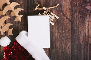 List of gifts with santa claus hat, cardboard fir trees and sleigh on the table top view photo