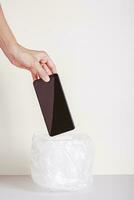 Hand throws smartphone into trash can for digital detox vertical view photo