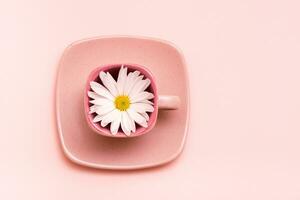 Pink concept. Empty square coffee cup with flower on saucer on pink background. Top view photo