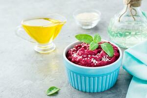 Baked beet hummus in a bowl with sesame seeds and basil on the table. Close-up photo