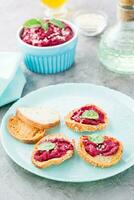 Homemade bruschetta with beetroot hummus on small baked baguette toast on a plate and a bowl of hummus on the table. Vertical view photo