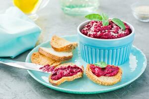 Homemade bruschetta with beetroot hummus on small toast on a plate and a table knife on the table photo