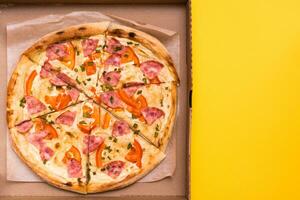 Takeaway and delivery. Ready-to-eat pizza in cardboard box on yellow background. Copy space photo