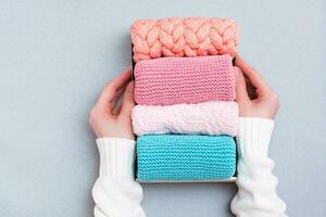 Organization and order. Women's hands hold a box of neatly folded knitted clothes. Top view photo