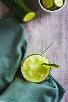 Detox cucumber lemonade in a glass with a straw and a cucumber on the table top and vertical view photo