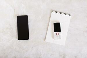 Modern smartphone and push-button phone on notepad on table top view photo