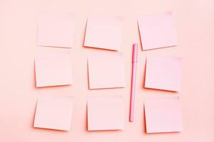 The concept is pink. Blank square small sheets of paper to write in even rows and a pen on a pink background. Top view photo