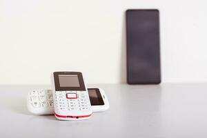 Two old-fashioned white push-button telephones lie on the table on the background of a smartphone photo