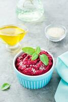Baked beet hummus in a bowl with sesame seeds and basil on the table. Vertical view photo