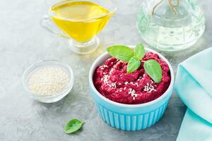 Baked beet hummus in a bowl with sesame seeds and basil on the table photo