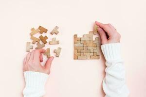 Organization and order. Female hands lay out wooden puzzle pieces on a pink background. Top view photo