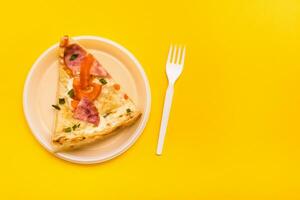 Takeaway and delivery. Pizza slice in disposable plastic plate and fork on yellow background photo