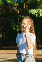 A girl in glasses happily talks on a push-button telephone among the trees vertical view photo