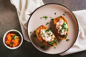 Close up of baked sweet potato stuffed with ricotta, tomatoes and herbs on a plate top view photo